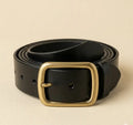 Black leather belt with a gold buckle on a beige background
