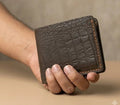 Brown leather wallet held in a hand against a neutral background