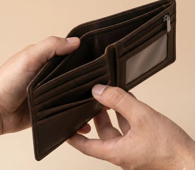 Brown leather wallet held open by a hand on a beige background