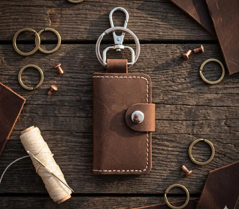 Brown leather keychain with metal clip on a wooden surface with tools and materials.