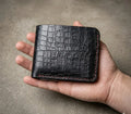 Hand holding a black crocodile skin wallet against a neutral background