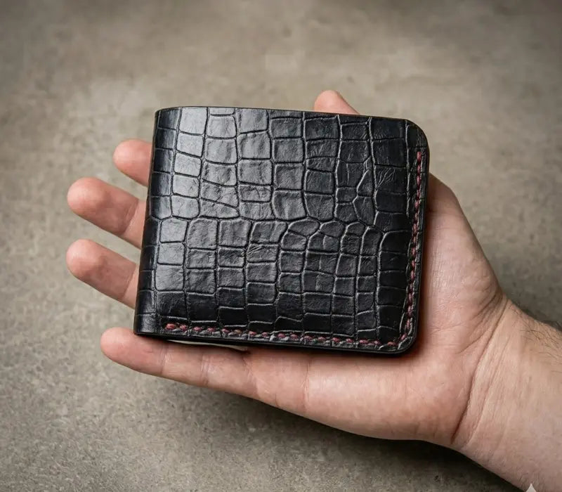 Hand holding a black crocodile skin wallet against a neutral background