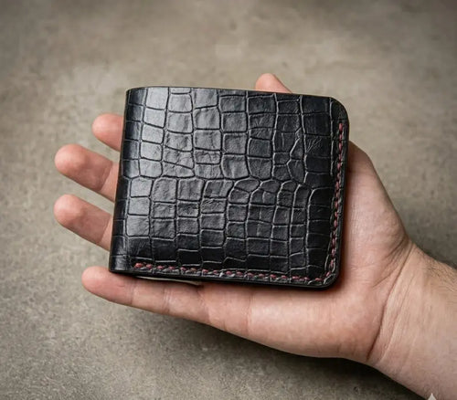 Hand holding a black crocodile skin wallet against a neutral background