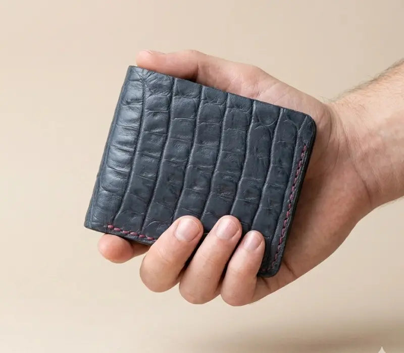 Navy blue croc-embossed handmade leather bifold wallet with burgundy stitching on a beige background
