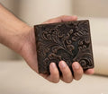 Hand holding a brown leather wallet with intricate floral patterns against a neutral background
