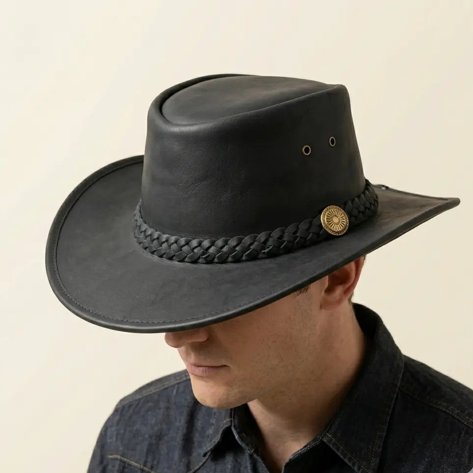 Man wearing a black leather hat with braided band and gold buckle on a beige background