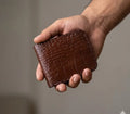 Hand holding a brown leather wallet with a textured pattern against a neutral background