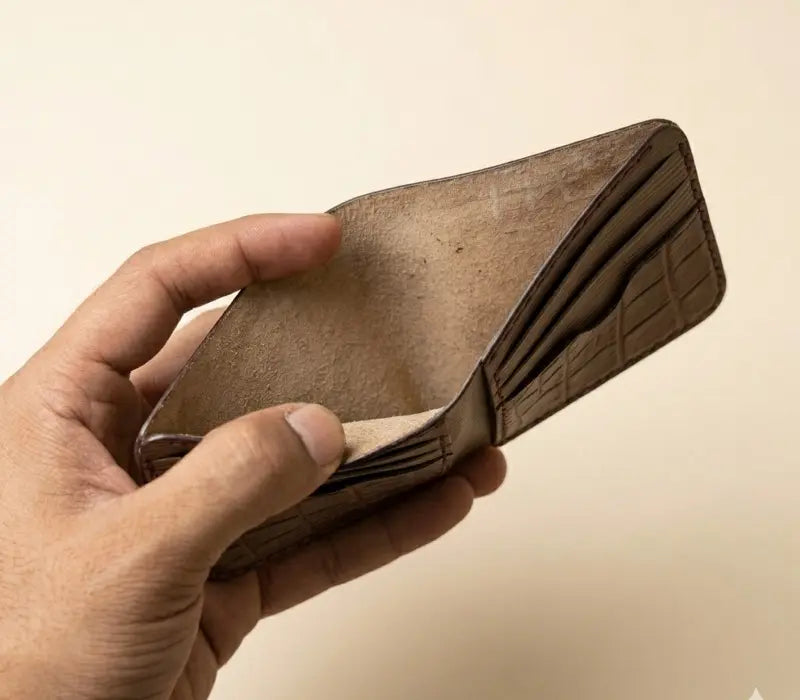 Hand holding a brown leather wallet against a beige background