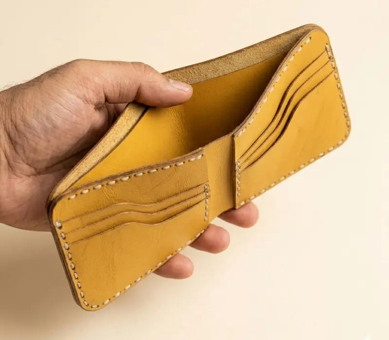Hand holding a yellow leather wallet against a beige background