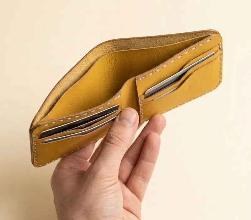 Hand holding a yellow leather wallet against a beige background