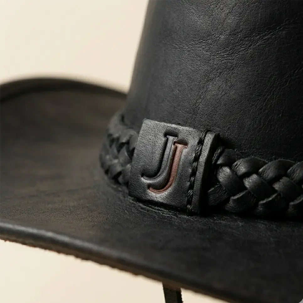 Close-up of a black leather cowboy hat with braided band and logo on a beige background