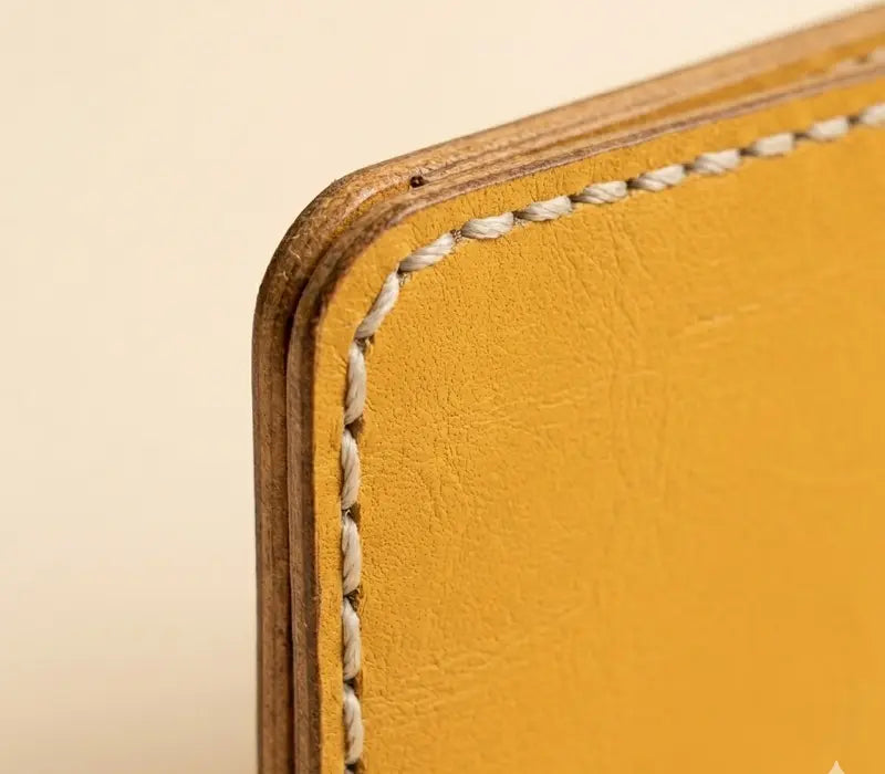 Close-up of a yellow leather product with visible stitching on a beige background