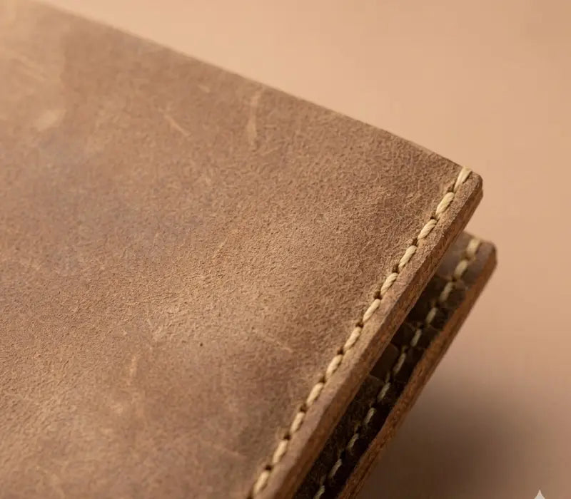 Close-up of a brown leather wallet with visible stitching on a beige background