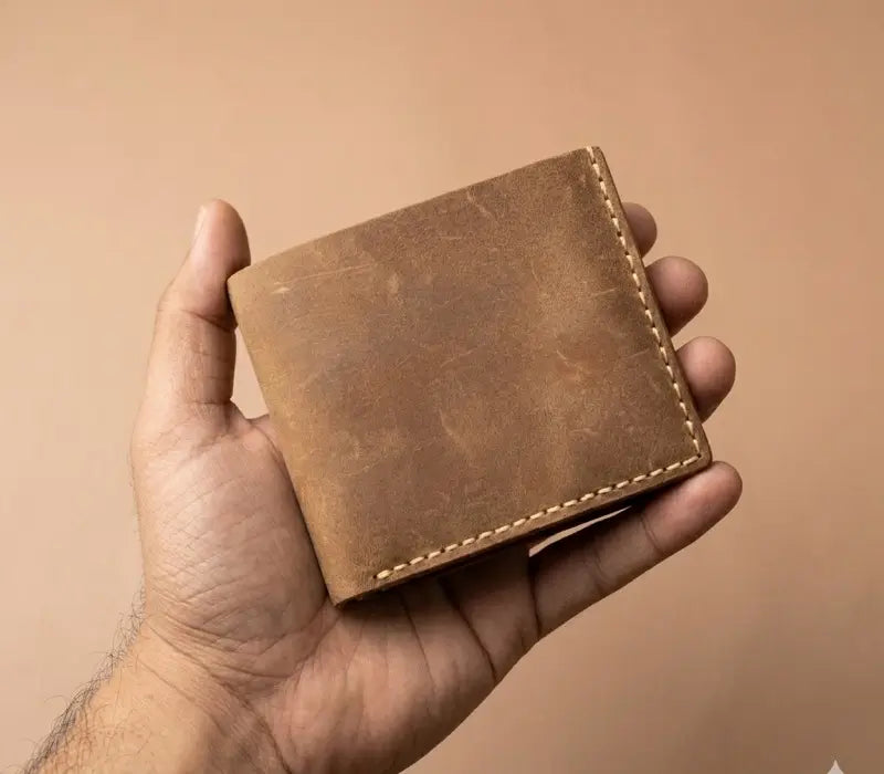 Brown leather wallet held in a hand against a beige background