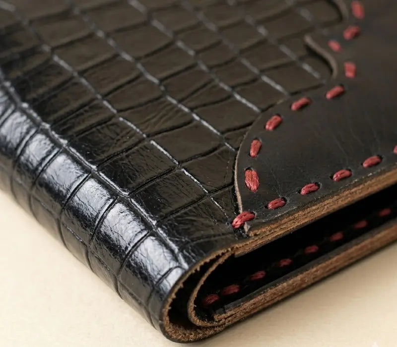 Close-up of a black leather wallet with red stitching on a beige background