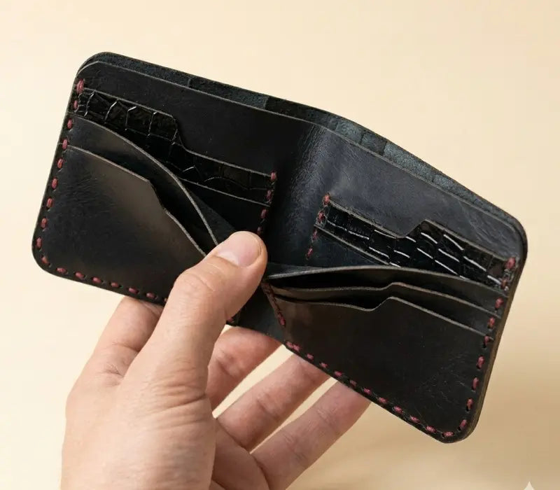 Hand holding a black leather wallet with red stitching on a beige background