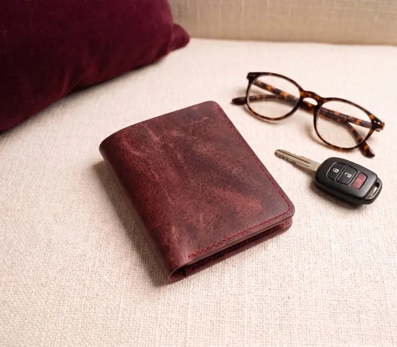Brown leather wallet, glasses, and car key fob on a beige surface