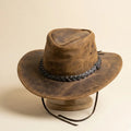 Brown leather cowboy hat with braided band on a beige background