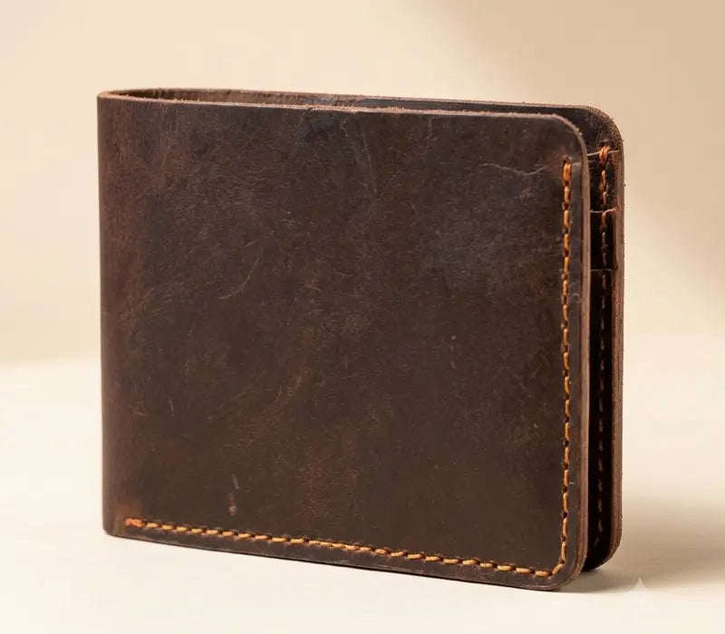 Dark brown full-grain handmade leather bifold wallet with hand-stitched edges on a beige background