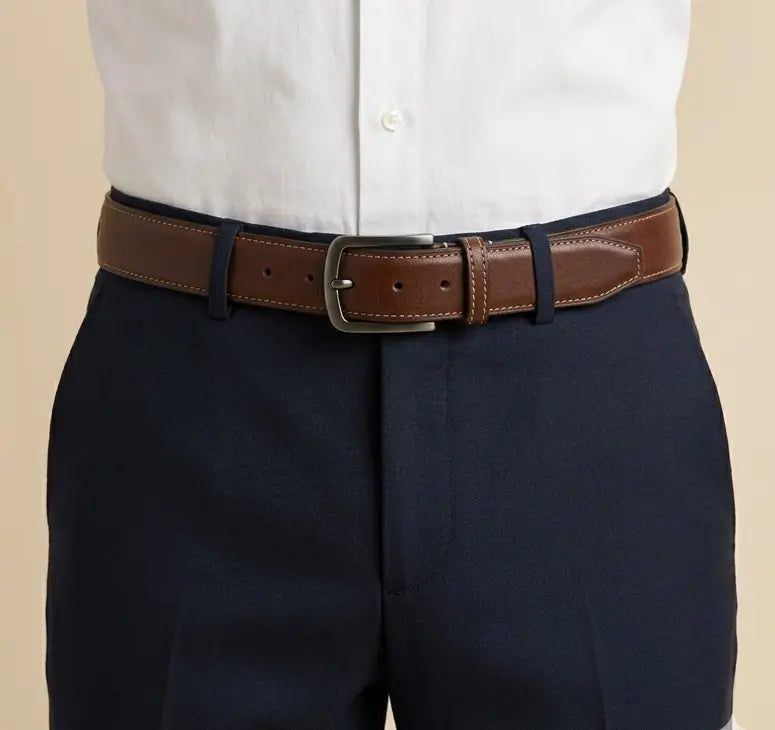 Brown belt with silver buckle worn by a person in navy pants and a white shirt on a beige background