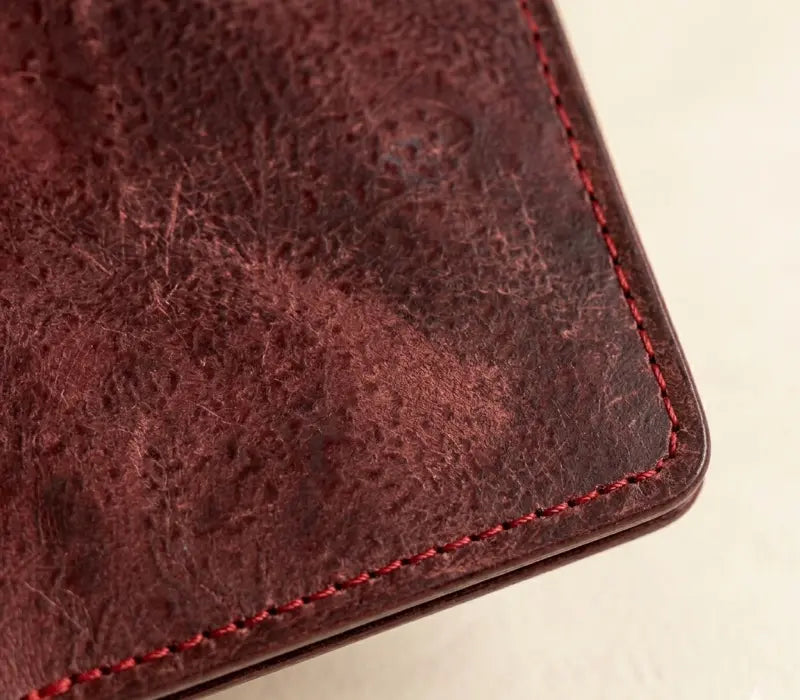 Close-up of a brown leather wallet with red stitching on a light background