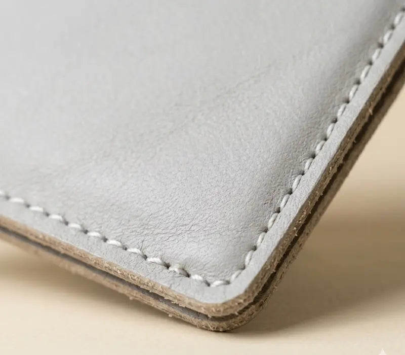 Close-up of a light gray leather wallet with white stitching on a beige background