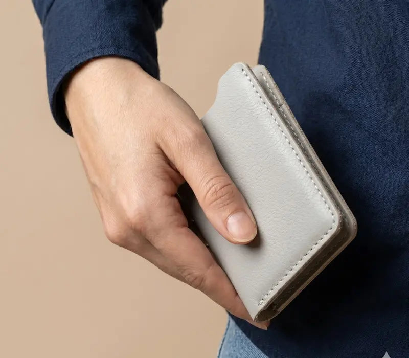 Hand holding a light gray wallet against a beige background