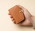Hand holding a brown leather wallet with a gold button on a beige background