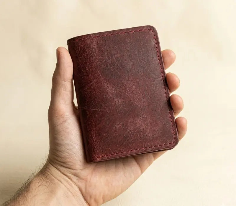 Hand holding a brown leather wallet against a beige background