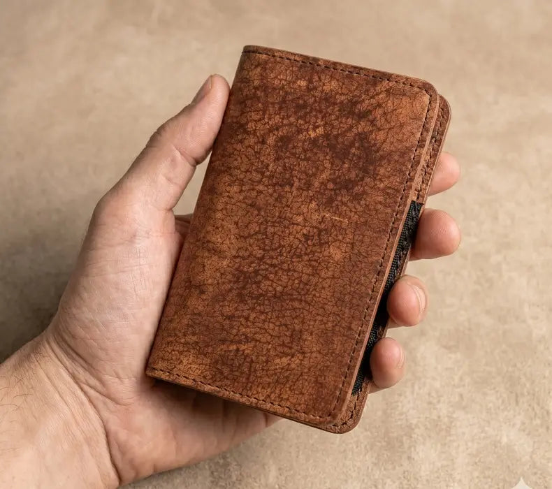 Hand holding a brown leather wallet against a beige background