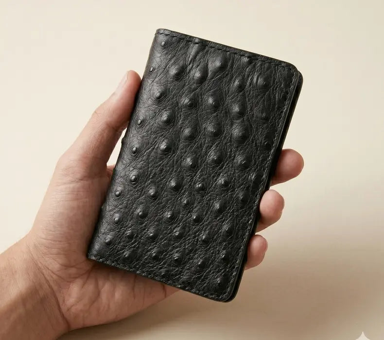 Hand holding a textured black leather wallet against a beige background