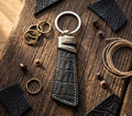 Black leather keychain with silver ring on a wooden surface with jewelry items.