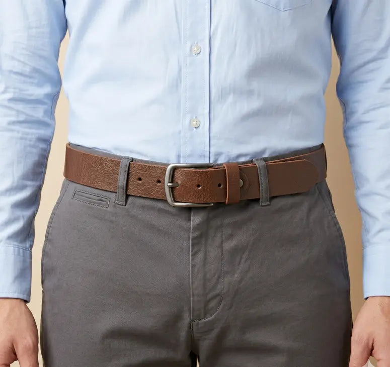 Person wearing a light blue shirt, gray pants, and a brown belt with a beige background