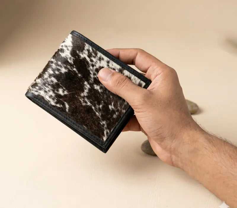 Hand holding a wallet with a cowhide pattern against a beige background