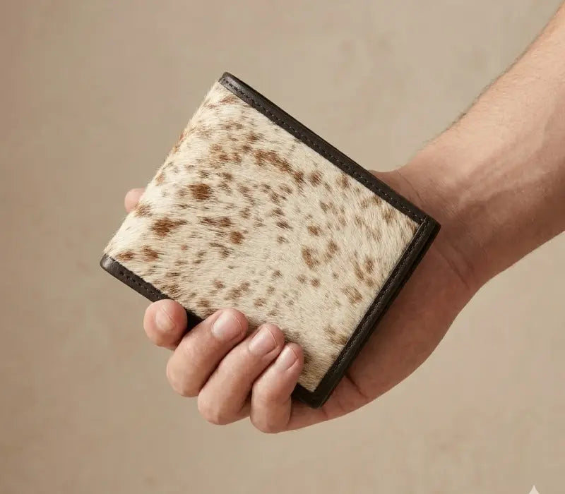 Hand holding a cowhide leather wallet against a beige background