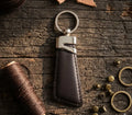 Brown leather keychain with metal clip on a wooden surface with sewing materials.