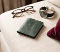 Green leather wallet, glasses, and watch on a textured surface