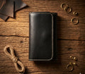 Black leather wallet on a wooden surface with gold rings and string