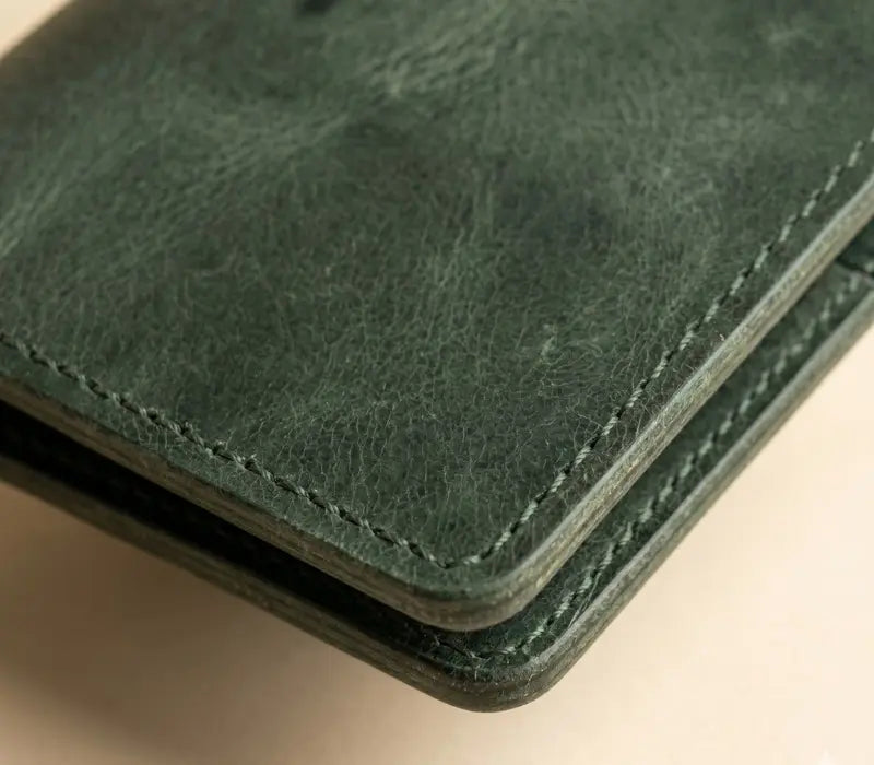 Close-up of a green leather wallet with visible stitching on a beige background