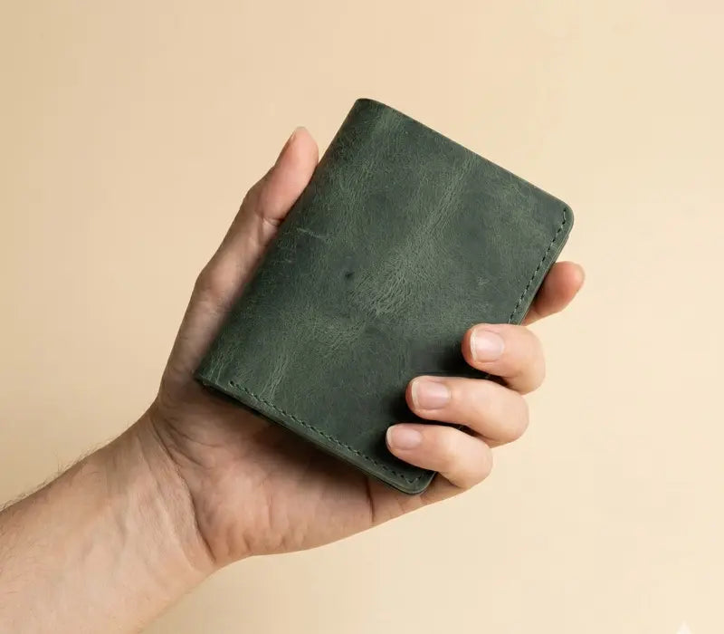 Hand holding a green leather wallet against a beige background