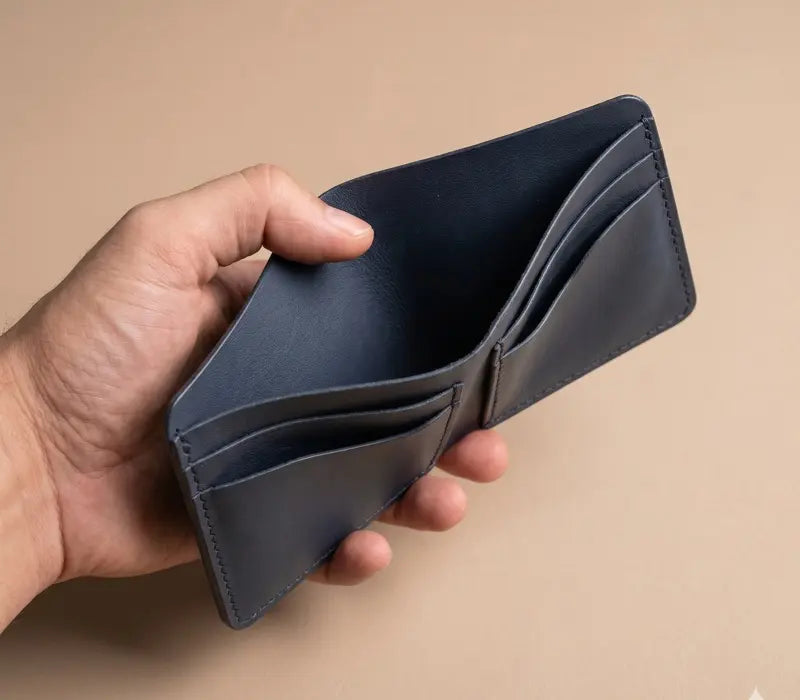 Hand holding an open blue leather wallet against a beige background