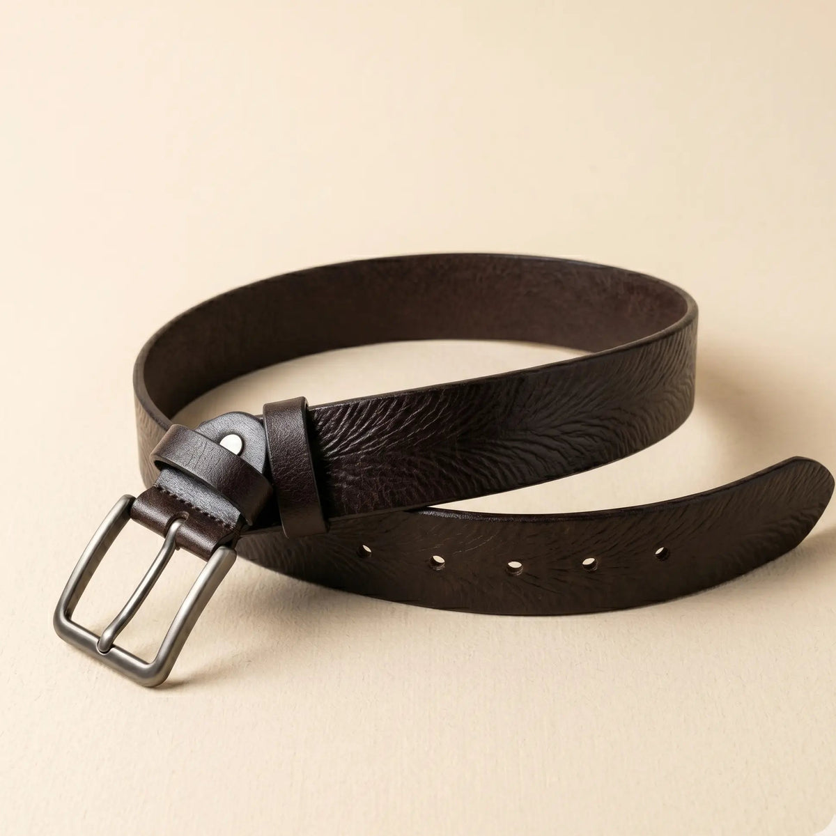 Brown leather belt with a silver buckle on a beige background