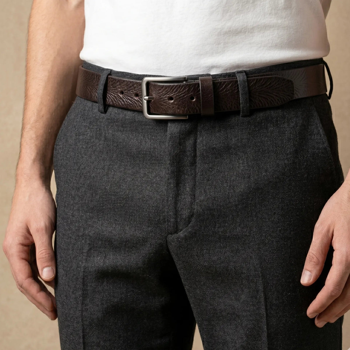 Person wearing gray pants with a brown belt on a beige background