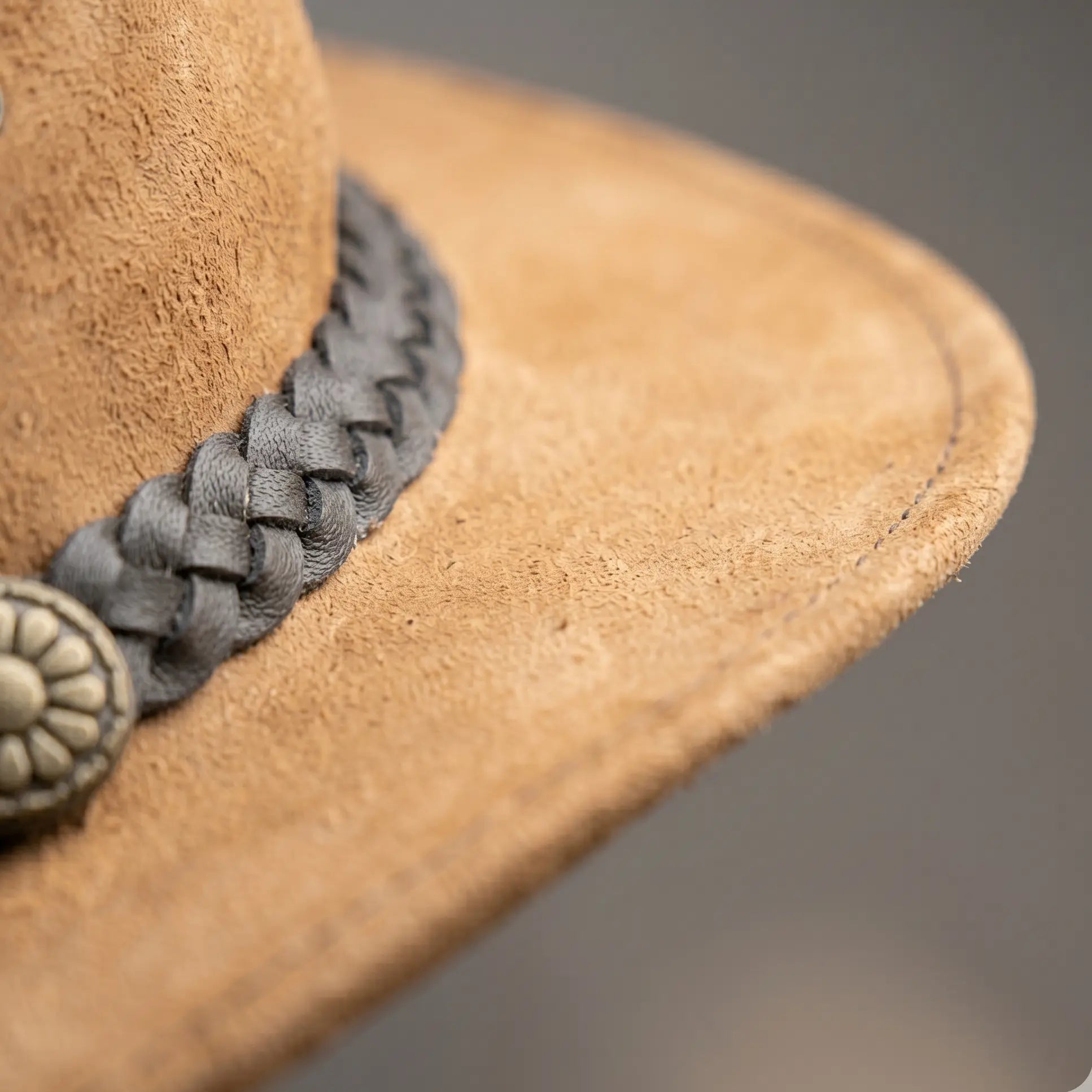 Close-up of a brown cowboy hat with a braided gray band and decorative button on a blurred background