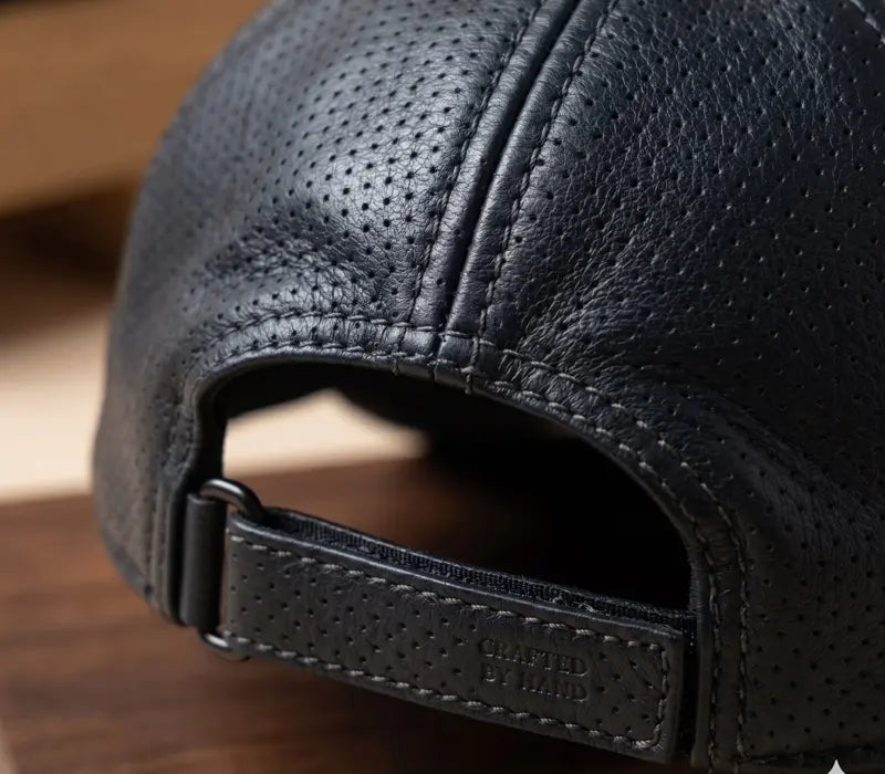 Close-up of a black leather cap with 'Crafted by Hand' label on a wooden surface