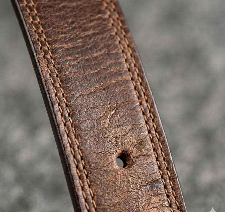 Close-up of a brown leather belt with visible stitching on a gray background