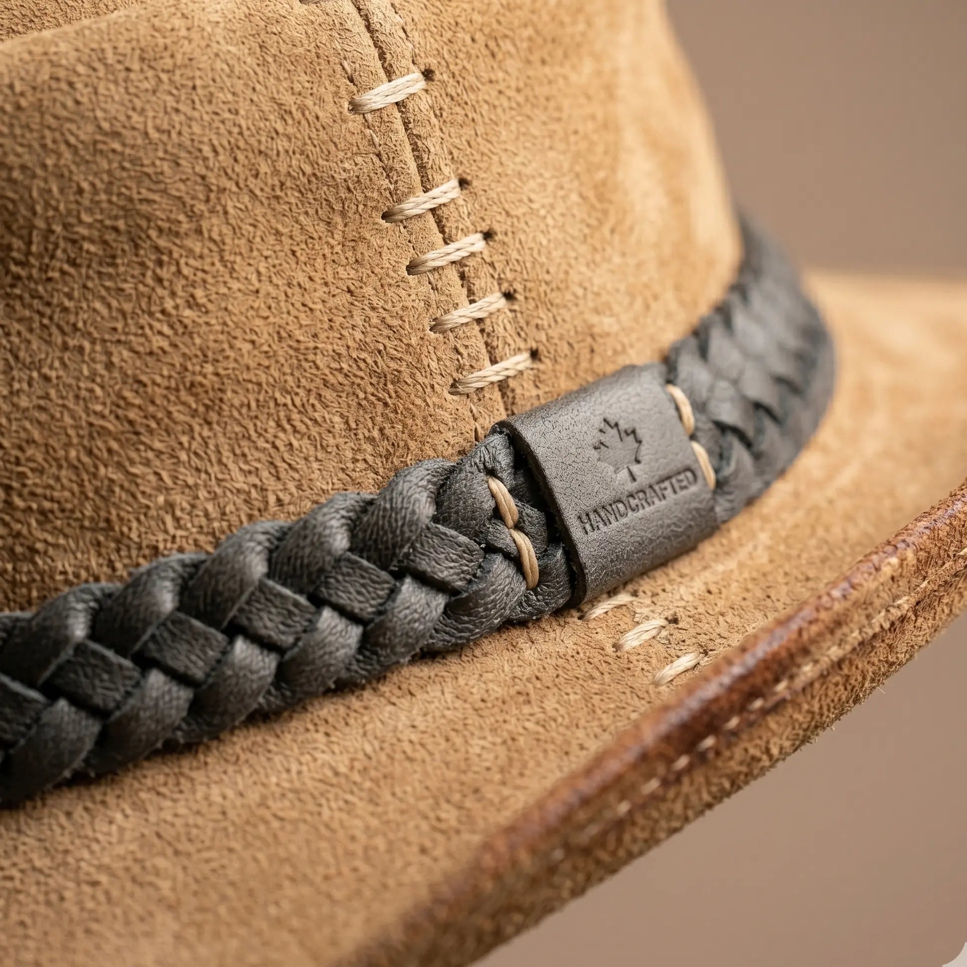 Close-up of a brown suede hat with a braided black leather band featuring a brand logo.