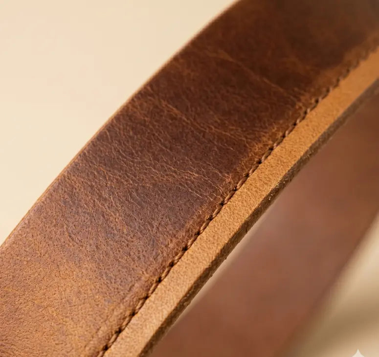 Close-up of a brown leather belt with visible stitching on a beige background