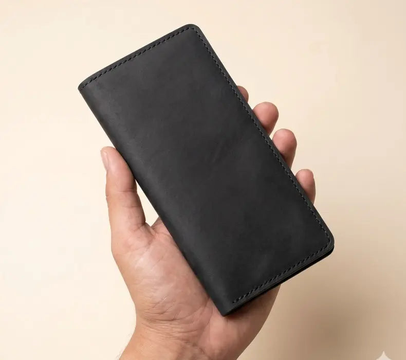 Hand holding a black leather wallet against a beige background