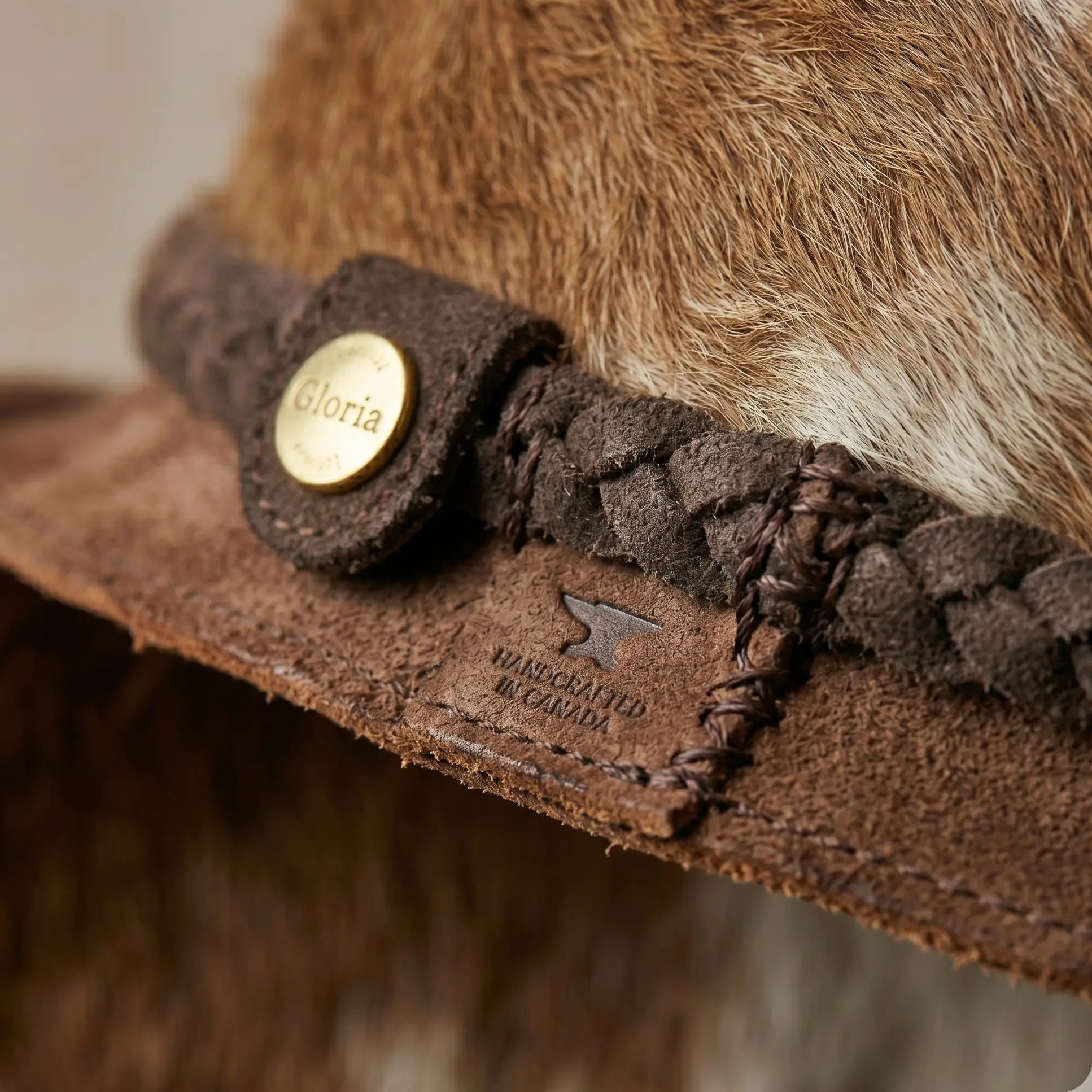 Close-up of a brown fur hat with braided band and 'Gloria' button, brand 'Baker & Taylor' visible.